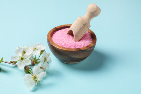 Sea salt in bowl, scoop and twigs with beautiful flowers on light blue backgroundの写真素材