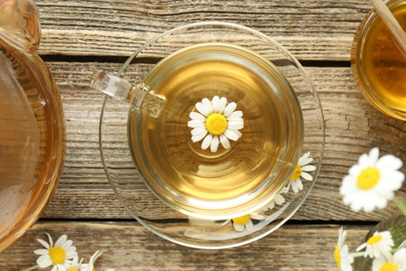 Delicious chamomile tea in glass cup, fresh flowers, honey and teapot on wooden table, flat layの写真素材