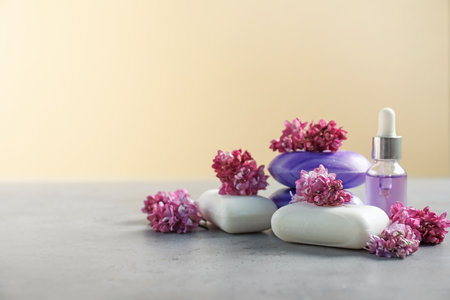 Soap bars, essential oil and lilac flowers on gray textured table against beige background, closeup. Space for textの写真素材