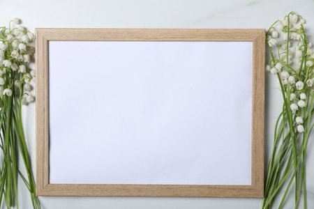 Beautiful lily-of-the-valley flowers and blank frame on white marble background, flat lay. Space for textの写真素材