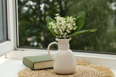 Bouquet of lily-of-the-valley flowers in vase and book on windowsill indoorsの写真素材
