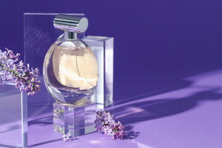 Stylish presentation of perfume bottle and lilac flowers on purple background, closeup. Space for...