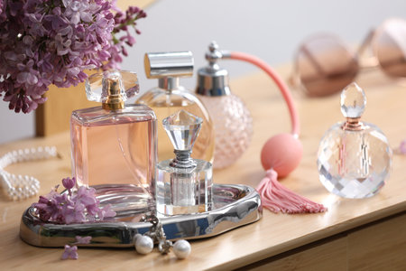 Bottles of perfumes, accessories and lilac flowers on wooden table, closeup