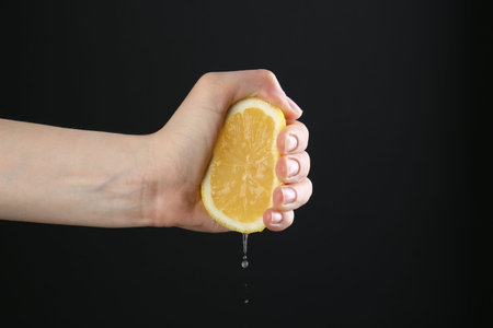 Woman squeezing lemon on black background, closeup