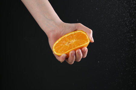 Woman squeezing orange on black background, closeup