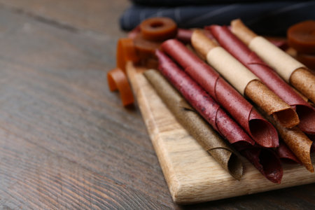 Tasty fruit leather rolls on wooden table, closeup. Space for textの写真素材