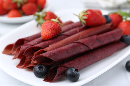 Tasty fruit leather rolls, strawberries and blueberries on white table, closeupの写真素材