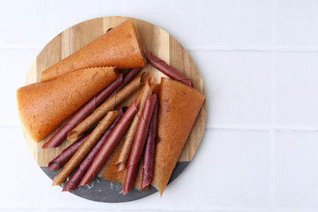 Fruit leather rolls on white tiled table, top view. Space for text