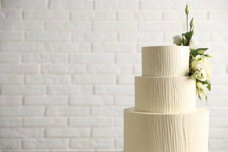 Delicious wedding cake decorated with flowers near white brick wall, closeup. Space for textの写真素材