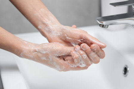 Woman washing hands at sink in bathroom, closeup