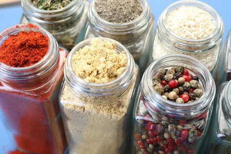 Different aromatic spices in jars on blue background, closeup