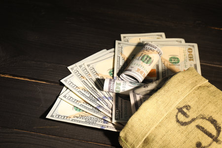 Money bag with dollar banknotes on black wooden table, closeupの写真素材