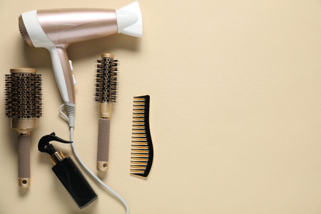 Round brushes, spray, comb and dryer on beige background, flat lay. Space for text