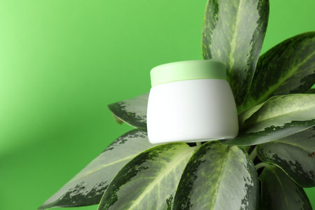 Jar of moisturizing body cream on plant against light green background, closeup. Space for textの写真素材