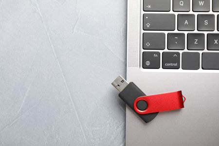 Modern flash drive and laptop on light grey table, top view. Space for text