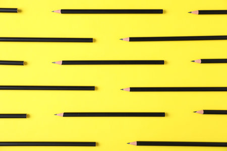 Many sharp graphite pencils on yellow background, flat lay