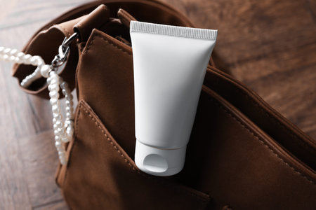 Tube of moisturizing body cream and leather bag on wooden table, closeupの写真素材