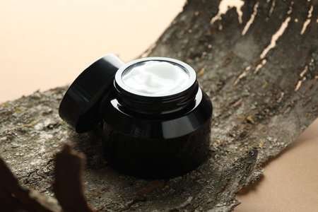 Jar of body cream and tree bark on beige background, closeup