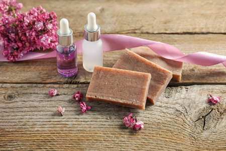 Soap bars, essential oil and lilac flowers on wooden table