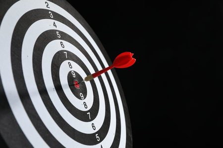 Targeting. Dart board with arrow on black background, closeup. Space for text
