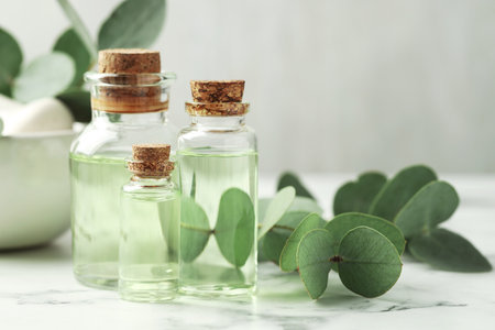 Bottles of essential oil and eucalyptus leaves on white marble table, closeupの写真素材