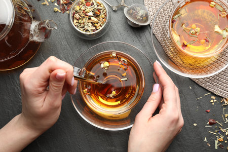 Woman with aromatic herbal tea at black table, top view