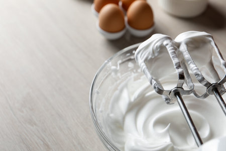 Hand mixer with whisks and whipped cream on wooden table, closeup. Space for textの写真素材