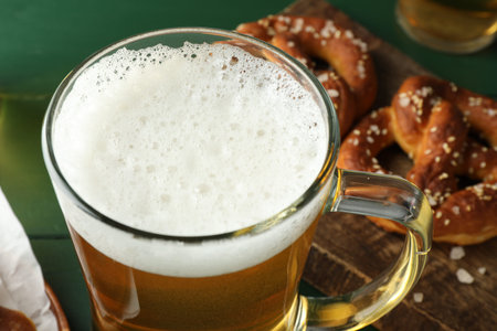 Glass of beer and tasty pretzels on green table, selective focusの写真素材