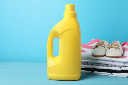 Bottle of fabric softener, stacked baby clothes and shoes on light blue backgroundの写真素材