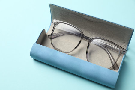 Case with stylish glasses on light blue background, closeup