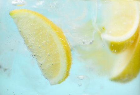 Refreshing soda water with slices of lemon and ice in glass on light blue background, closeupの写真素材