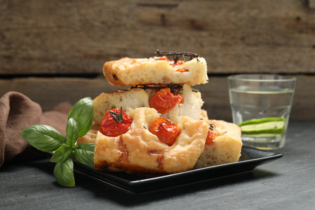 Pieces of delicious focaccia with tomatoes, basil and glass of water on gray tableの写真素材