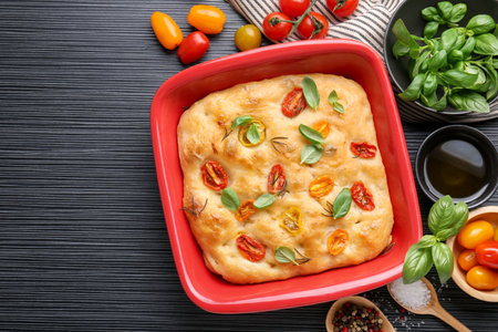 Delicious focaccia with tomatoes, spices and oil on black wooden table, flat layの写真素材