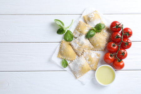 Uncooked ravioli, basil, tomatoes and oil on white wooden table, flat lay. Space for textの写真素材