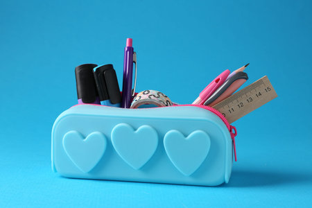 Different stationery in pencil case on light blue background, closeup