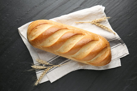 Loaf of bread and spikes on black textured table, flat lay