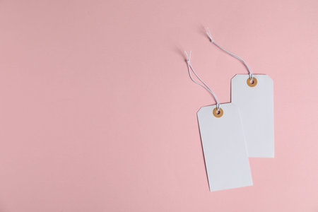 Blank tags with strings on pink background, flat lay. Space for text