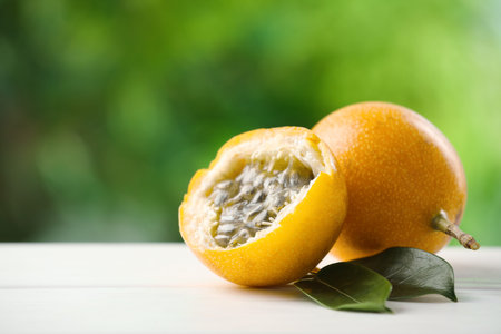 Ripe passion fruits and green leaves on white wooden table outdoors, closeup. Space for text