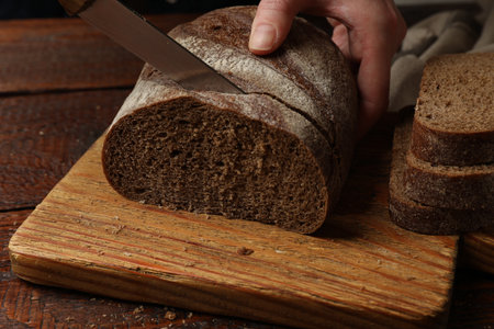 Woman cutting fresh bread at wooden table, closeupの写真素材