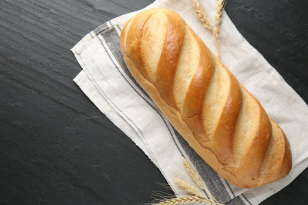 Loaf of bread and spikes on black textured table, flat lay. Space for text