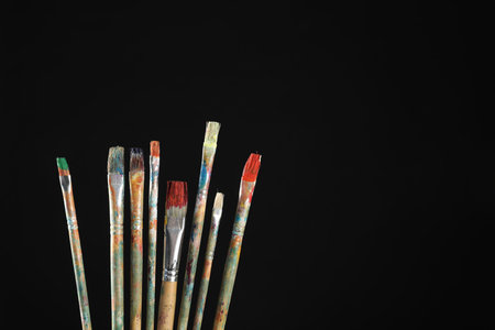Many dirty paintbrushes on black background, closeup. Space for text