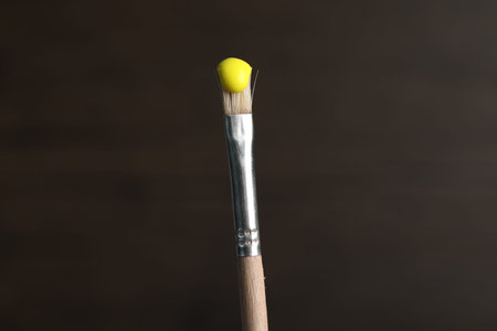 Brush with yellow paint on wooden background, closeup