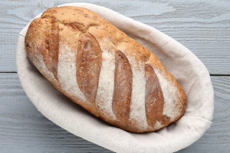 Loaf of bread in basket on grey wooden table, top view