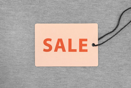 Tag with word Sale on grey fabric, top view