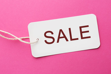 White tag with word Sale on pink background, top view