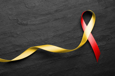World Hepatitis Day. Yellow-red awareness ribbon on black table, top viewの写真素材