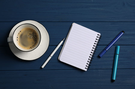 Notebook with pen, markers and coffee on blue wooden table, flat layの写真素材