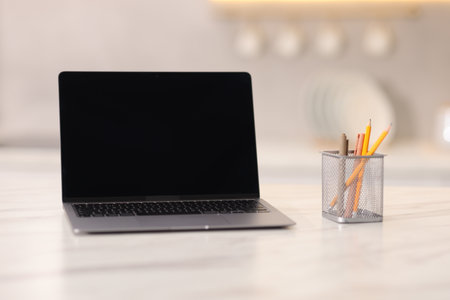 Laptop with blank screen and stationery on white marble table in kitchen. Mockup for designの写真素材