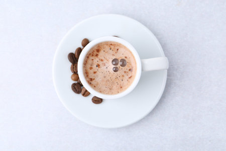Aromatic coffee in cup, beans and saucer on light table, top view