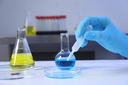 Scientist taking sample with pipette out of Petri dish at table in laboratory, closeupの写真素材